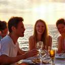 A group of friends laughing and dining al fresco on a yacht, representing a successful group charter.